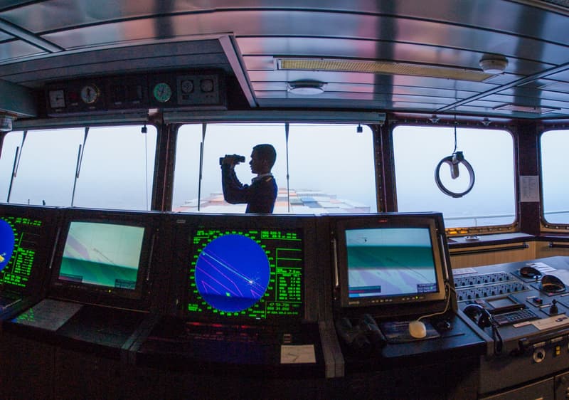 Navigation officer keeping watch with binoculars on the bridge of a cargo ship