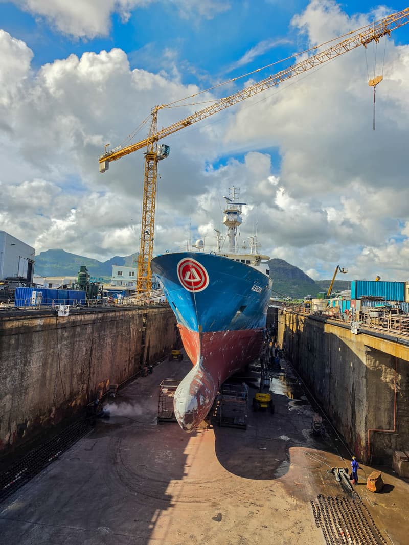 Cargo ship in a shipyard dry dock beneath a tower crane